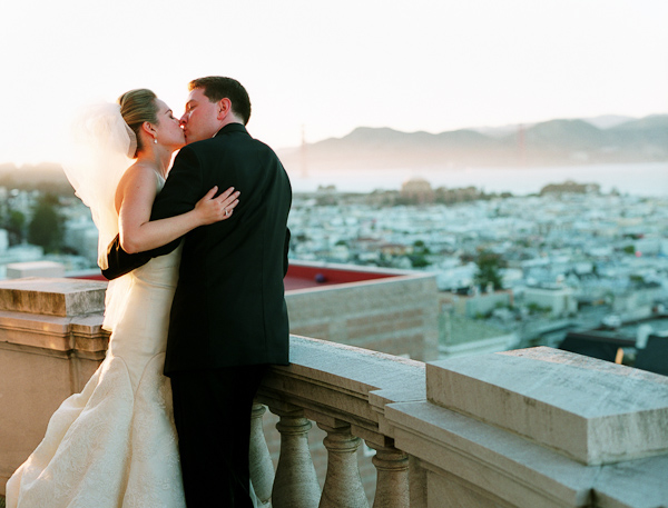the happy couple kissing on balcony overlooking city - photo by San Francisco based wedding photographer Lisa Lefkowitz